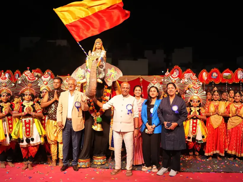 School management and guests on stage with costumed students and the Karnataka flag
