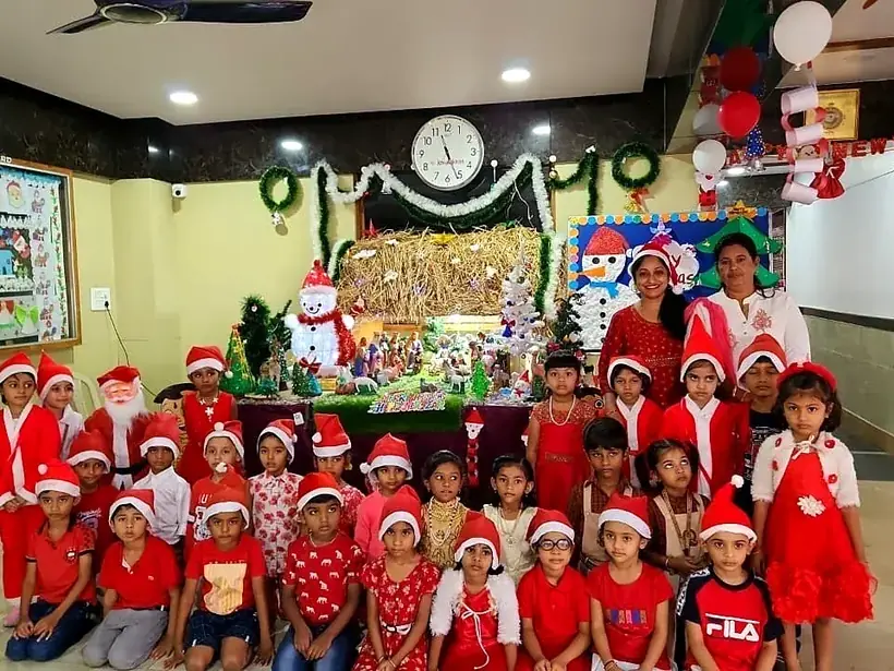Young children in Santa hats and red costumes celebrating Christmas in a decorated classroom