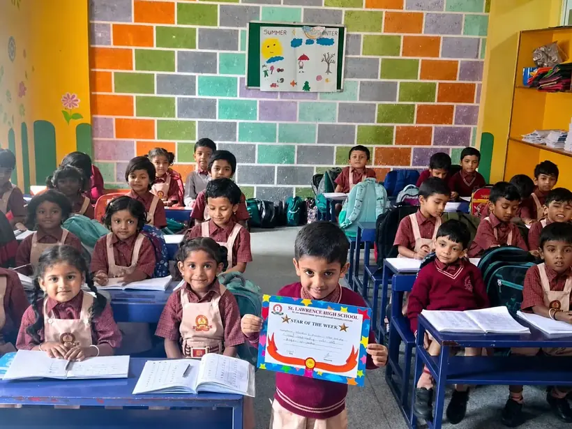 Primary students at their desks in a brightly decorated classroom, one holding a Star of the Week certificate
