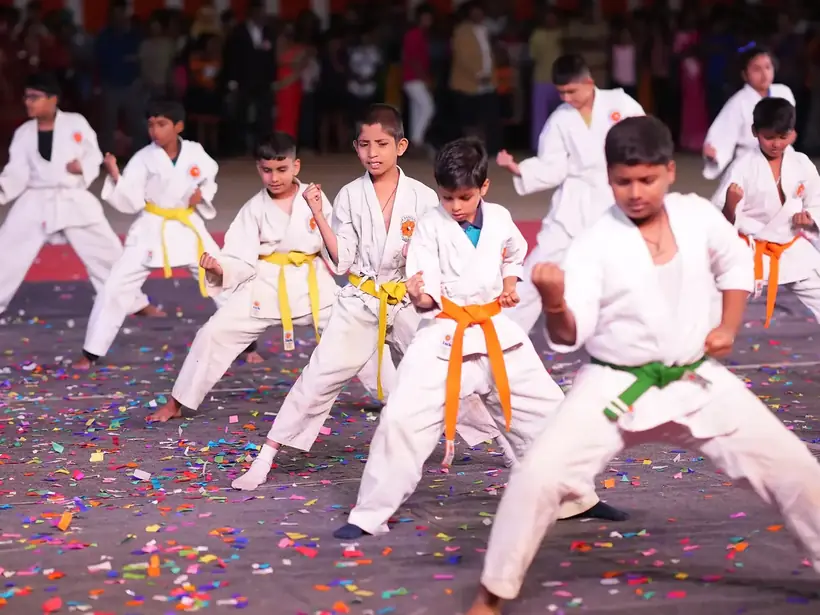 Students in karate uniforms with coloured belts performing a formation demonstration