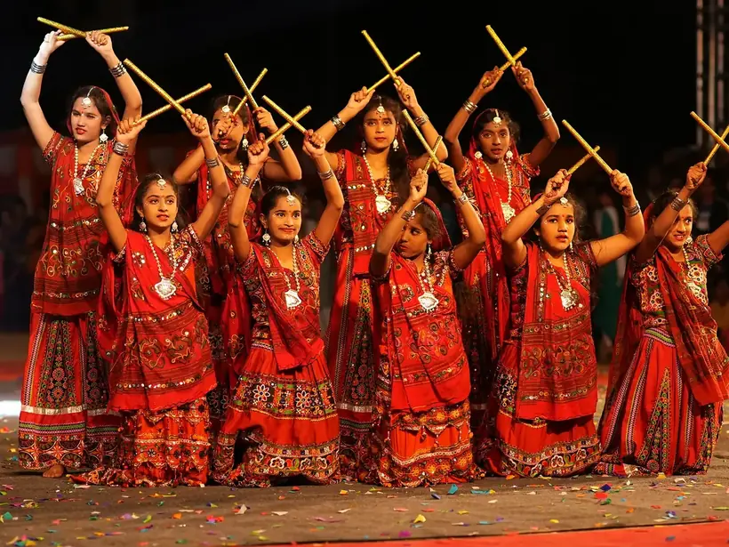 Girls in red traditional dress performing Kolattam, the stick dance, with raised sticks