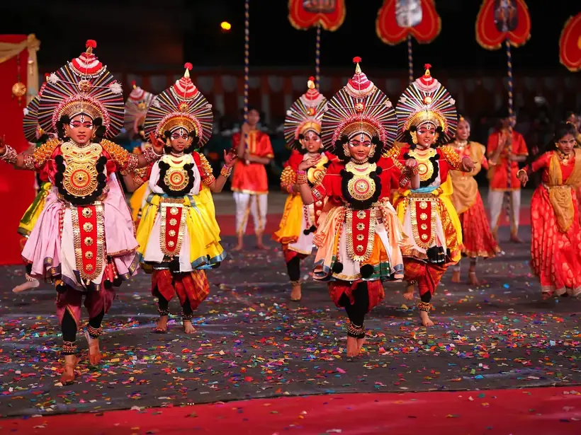 Students in elaborate Yakshagana costumes and headdresses performing on stage