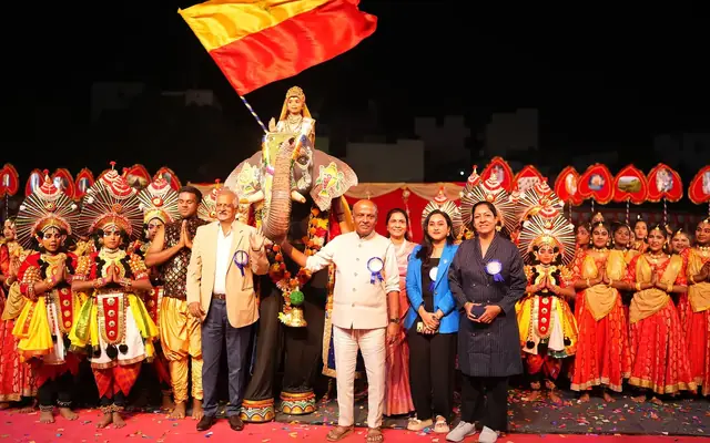 School management and guests on stage with costumed students and the Karnataka flag