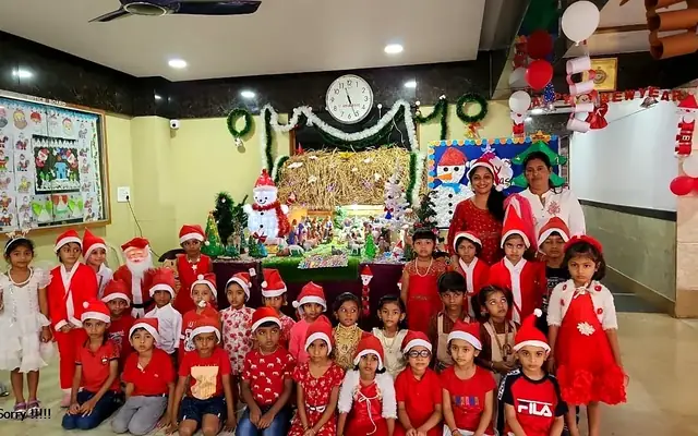 Young children in Santa hats and red costumes celebrating Christmas in a decorated classroom