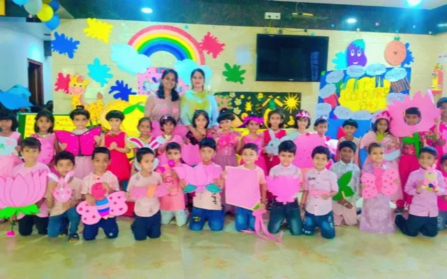 Kindergarten students dressed in pink holding pink paper craft cutouts — a lotus flower, butterflies and a rabbit — with a teacher for Colour’s Day