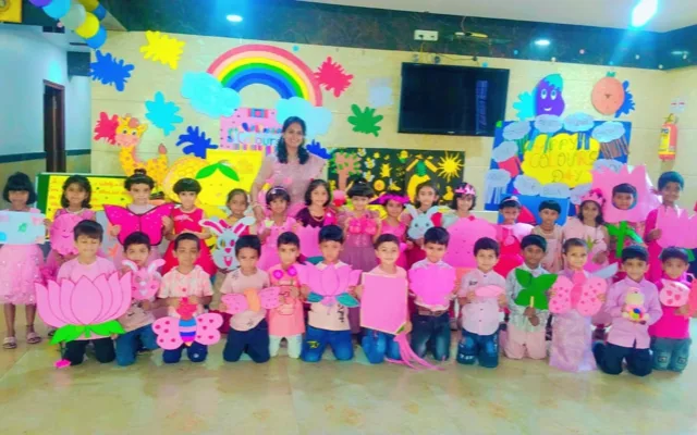 A teacher in pink standing with students holding pink lotus, tulip and butterfly cutouts for Colour’s Day
