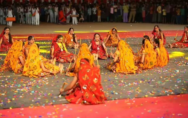 Students in bright ghagra costumes performing a seated formation dance