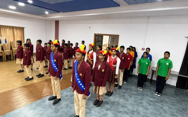 High school students in maroon blazers standing in formation at assembly, with house captains wearing sashes