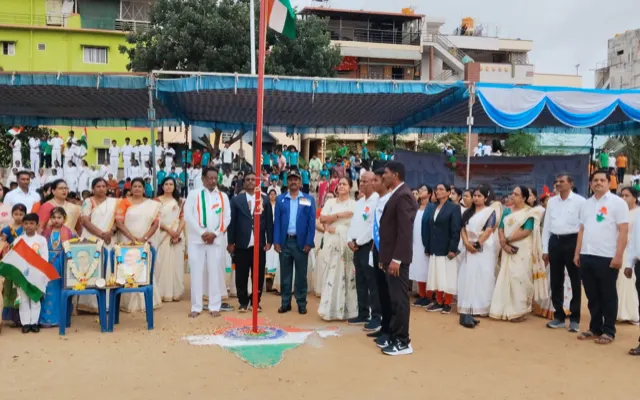 Students and staff standing to attention and saluting at the flag mast during the Independence Day ceremony