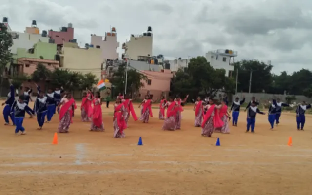 Large group of students in pink and blue folk costume performing a mass dance on the school ground