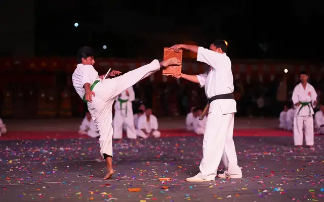A student performing a flying kick to break a board during a karate demonstration