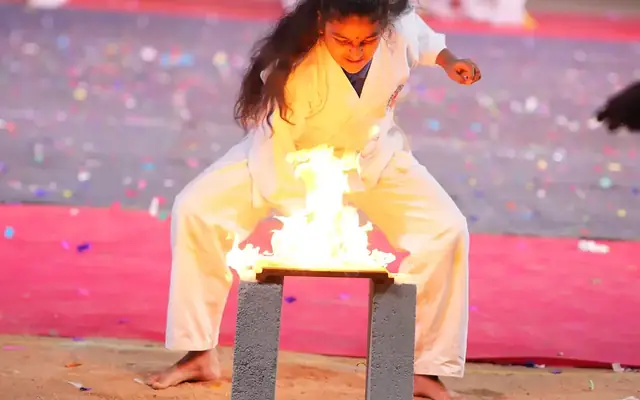 A student in karate uniform performing a breaking demonstration on stage