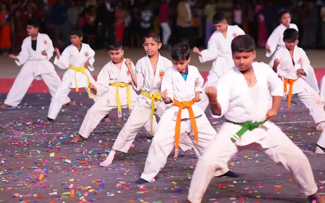 Students in karate uniforms with coloured belts performing a formation demonstration