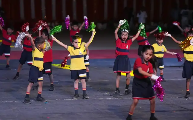 Young children in school uniform performing a stage display with pom-poms