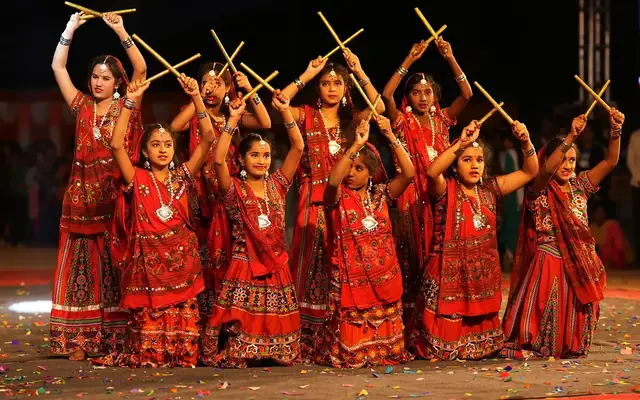 Girls in red traditional dress performing Kolattam, the stick dance, with raised sticks