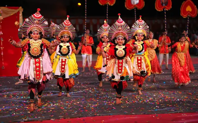 Students in elaborate Yakshagana costumes and headdresses performing on stage