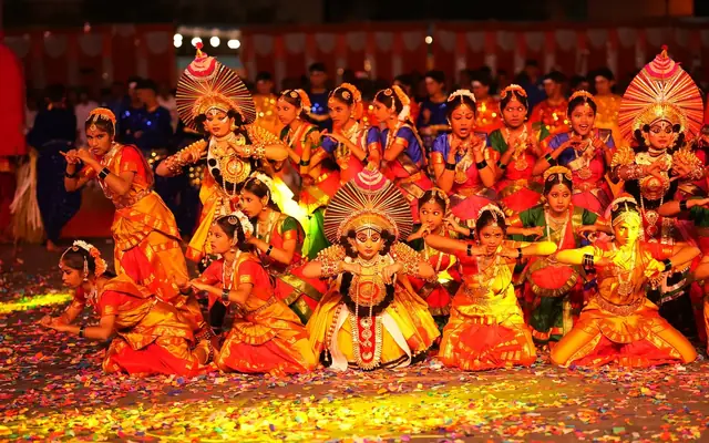 Students in ornate traditional costume performing a group dance under stage lights