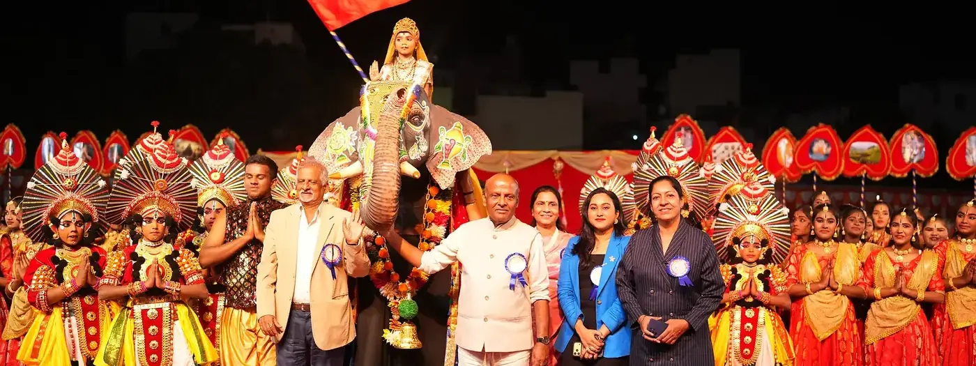 School management and guests on stage with costumed students and the Karnataka flag