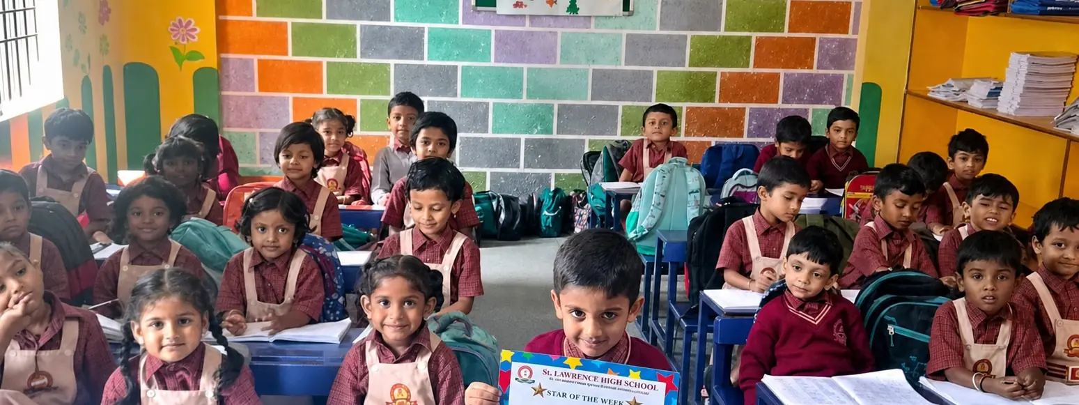 Primary students at their desks in a brightly decorated classroom, one holding a Star of the Week certificate