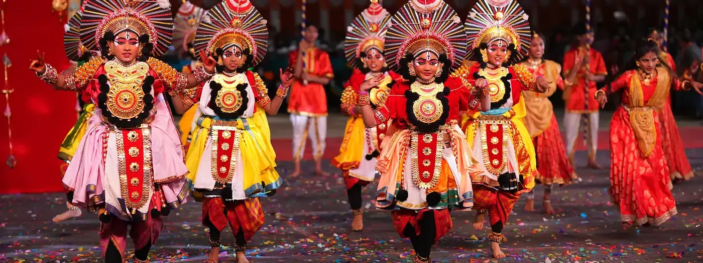Students in elaborate Yakshagana costumes and headdresses performing on stage